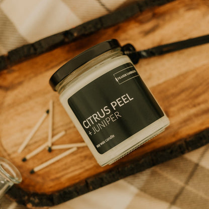 soy wax candle with citrus peel and juniper scent notes in a 9 oz glass jar next to some wooden matches
